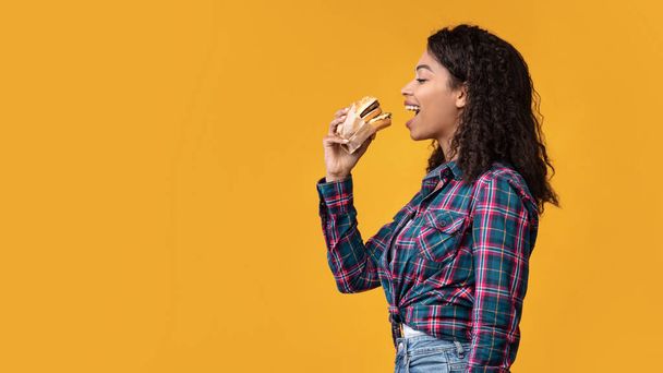 Divertida dama afroamericana comiendo hamburguesa en el estudio - Foto, Imagen