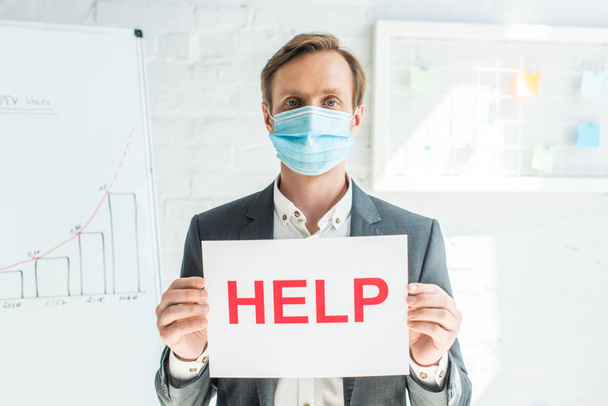 Front view of businessman holding sign with help lettering, while standing near flipchart on blurred background - Photo, Image