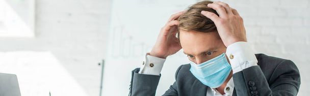 Бизнесмен в медицинской маске держит руки возле головы с размытым флипчартом на заднем плане, баннер - Фото, изображение