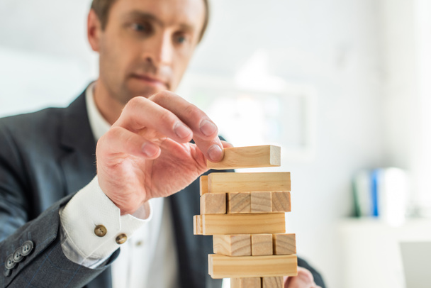 Concentrated businessman playing blocks wood game on blurred background - Photo, image