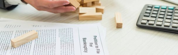 Cropped view of businessman with hand near block wood game falling near petition for bankruptcy at workplace, banner - Photo, Image