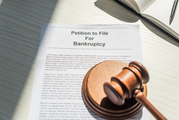Gavel with wooden block on petition for bankruptcy near blank notebook on white textured background - Photo, Image