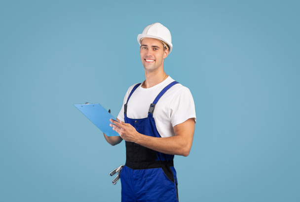 Repair And Renovation. Smiling handyman in hard hat posing over blue background - Photo, Image