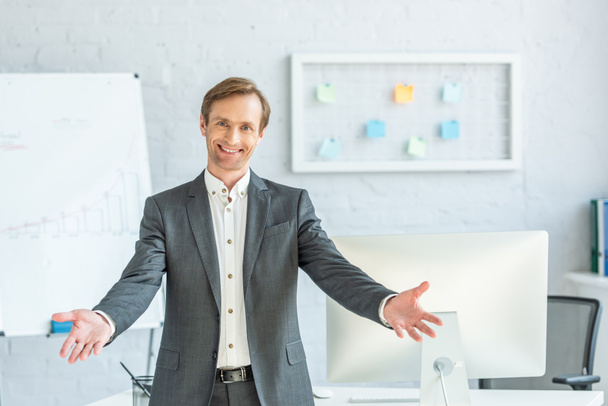 Front view of happy businessman with open arms looking at camera with blurred office on background - Photo, Image