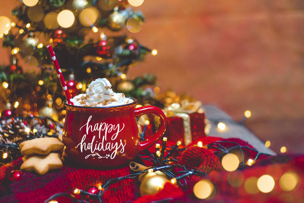 Punainen muki kuumaa kahvia jouluvaloilla, tuoreilla kekseillä, kermalla, kanelilla ja oljilla - Valokuva, kuva