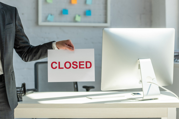 Cropped view of businessman holding sign with closed lettering with blurred workplace on background - Фото, зображення