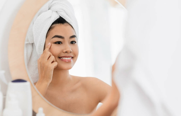 Cheerful asian woman applying eye cream at home - Photo, Image