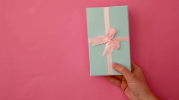Wystarczy zaprojektować kobiecą rękę trzymając niebieskie pudełko odizolowane na różowym pastelowym kolorowym modnym tle. Boże Narodzenie Nowy Rok urodziny walentynki prezentują romantyczny pomysł. Przestrzeń kopiowania - Materiał filmowy, wideo