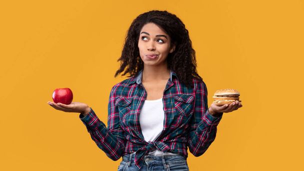 Éhes fekete hölgy kezében Burger és alma gyümölcs - Fotó, kép