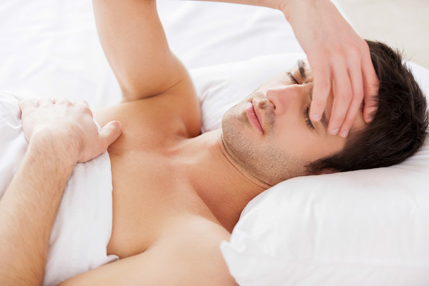 Homem segurando a mão no cabelo e mantendo os olhos fechados enquanto deitado na cama
 - Foto, Imagem
