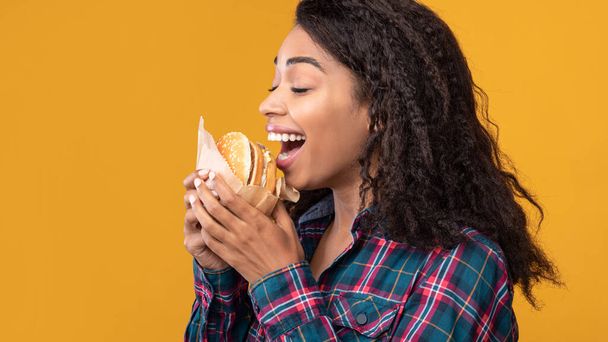 面白いアフリカ系アメリカ人女性がスタジオでバーガーを食べる - 写真・画像