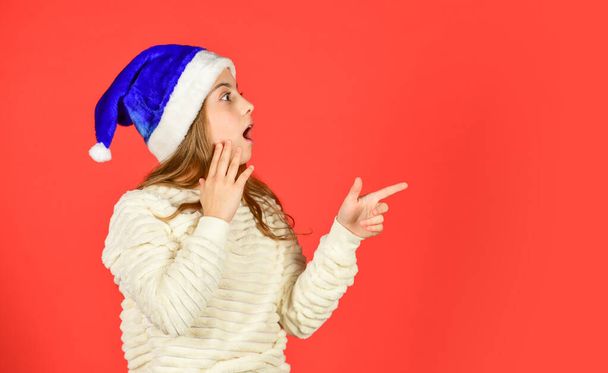 Christmas holiday invitation. Adorable girl wear santa claus hat red background. Emotional face expression. Happy childhood. Counting days till christmas. Christmas party. Can not hold back emotions - Photo, image