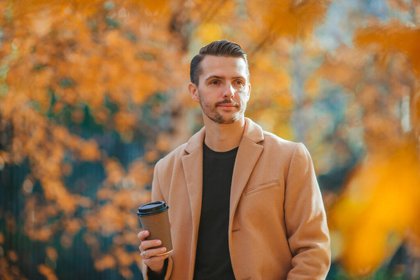 Молодой человек пьет кофе на природе в осеннем парке - Фото, изображение