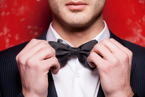 Handsome young man in formalwear adjusting his bow tie - Foto, afbeelding