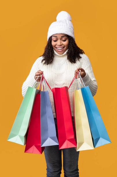 Junge schwarze Dame hält Einkaufstüten und schaut hinein - Foto, Bild
