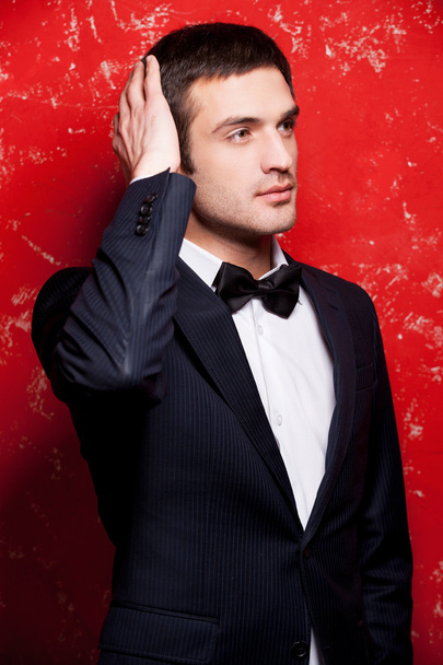 Man in suit and bow tie touching his hair and looking away - Foto, imagen