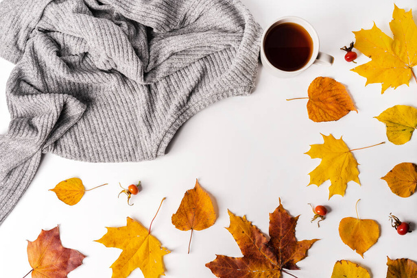 Осенняя композиция на белом фоне с кленовыми листьями, свитером и чашкой чая. Осенняя концепция домашнего комфорта, пространство для копирования - Фото, изображение
