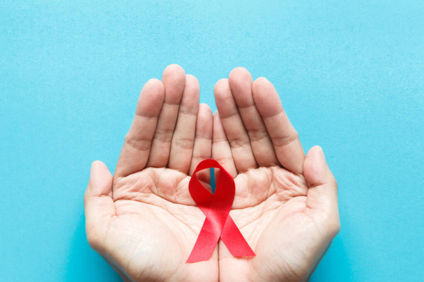 nastro di sensibilizzazione all'AIDS rosso sulla mano con sfondo di carta blu. Giornata mondiale degli aiuti e concetto di sanità e medicina - Foto, immagini