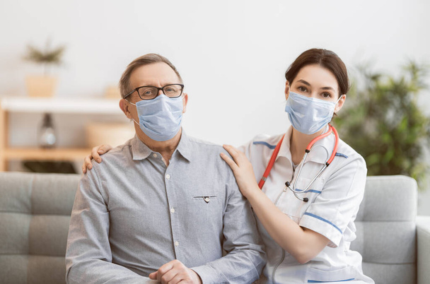 Doctor and senior man wearing facemasks during coronavirus and flu outbreak. Virus and illness protection, home quarantine. COVID-2019 - Foto, afbeelding