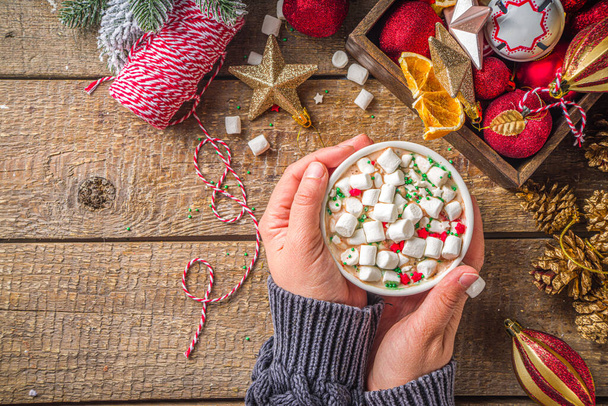 Heiße Schokolade mit Marshmallows, warmes Schokoladengetränk zum Frühstück am Weihnachtsmorgen, auf Holzgrund mit Weihnachtsdekoration, gemütliches Winterbild. Heiße Schokolade in Mädchenhänden  - Foto, Bild