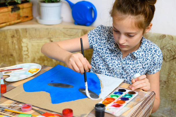 ένα κορίτσι που σχεδιάζει μπλε χαρτόνι γκουάς, καλλιτεχνική δημιουργία στο σπίτι, κάνει δημιουργικό έργο τέχνης - Φωτογραφία, εικόνα