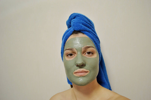 Donna con asciugamano blu sulla testa e maschera di argilla sul viso - Foto, immagini