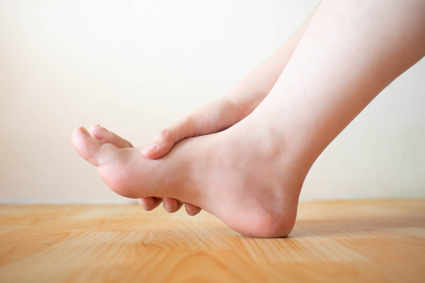 Young female suffering from foot pain or numbness at home. Causes of pain include plantar fasciitis, gout, arthritis, tendinitis, diabetic neuropathy or overuse injuries. Healthcare concept. Close up. - Photo, Image