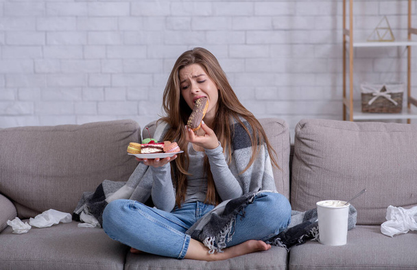 Kényelmes ételek és stressz evés koncepció. Frusztrált fiatal hölgy süteményt eszik otthon a kanapén. - Fotó, kép