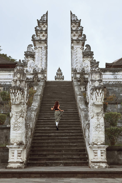 Young Woman Climbing Up Stone Stairs To Gates Of Heaven In Pura Lempuyang Temple In Bali, Indonesia. Beautiful Girl Walks And Explores Ancient Architecture In Karangasem, Asia. - Photo, Image