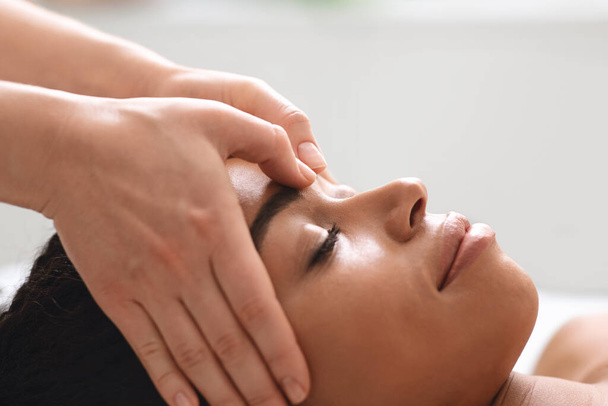 massage therapeut wrijven afrikaanse amerikaanse dame voorhoofd - Foto, afbeelding