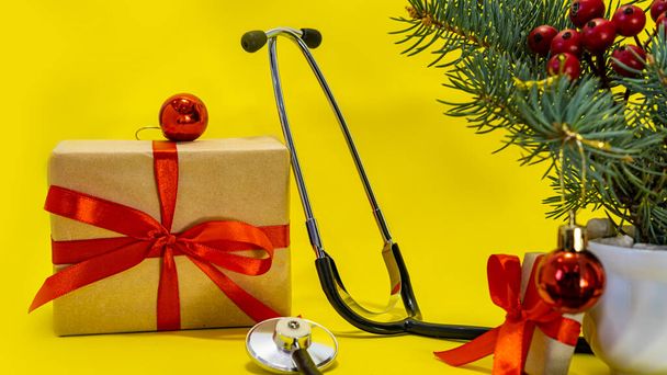 zdravotnický pracovník dovolená vánoční koncept, phonendoscope, vánoční strom, krabice s dárky, červené koule na žlutém pozadí, pro Nový rok banner - Fotografie, Obrázek