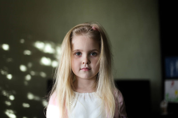 Gros plan portrait d'une petite fille blonde à la maison. Jolie fille de 5 ans avec de gros yeux et de longs cheveux srtaight regardant la caméra avec une expression sérieuse sur le visage. - Photo, image