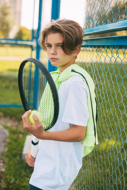 Portrait d'un beau adolescent debout avec une raquette de tennis et une balle dans les mains. Joueur de tennis au repos après l'entraînement. Sport, sportif, mode de vie, loisir - Photo, image