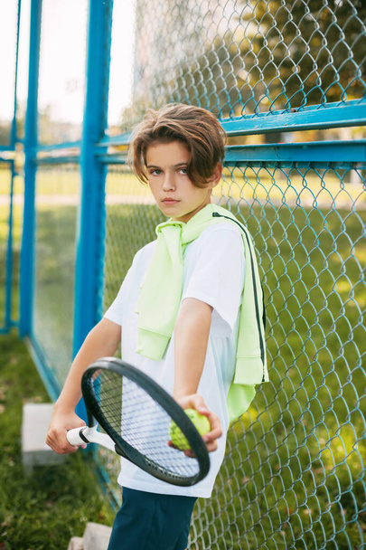 Portré egy gyönyörű tinédzser fiúról, aki teniszütővel és labdával a kezében áll. Teniszező pihenő edzés után. Sport, sportoló, életmód, szabadidő - Fotó, kép