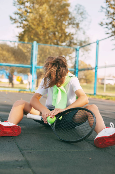 Słodki nastolatek siedzi na korcie tenisowym i odpoczywa po ciężkim treningu. Sport, sport, styl życia, wypoczynek - Zdjęcie, obraz