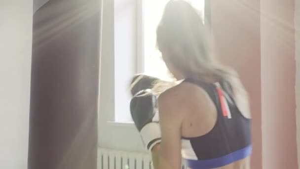 Női kickboxer üt boxzsák ringben, míg a por részecskék repül napkitörés fény háttér. - Felvétel, videó