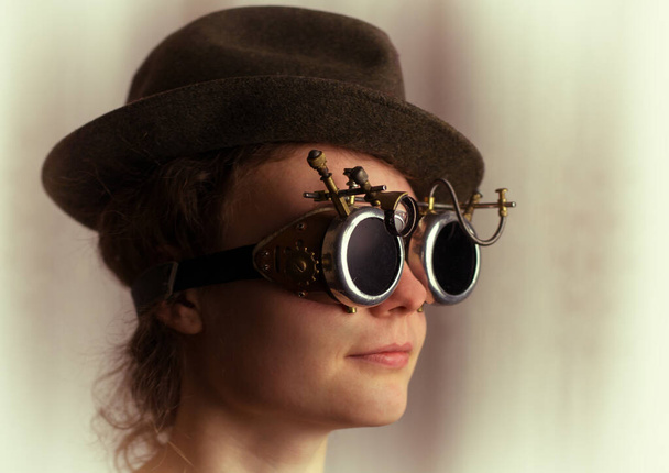 Portrait of attractive steampunk girl wearing googles and hat on light background - Photo, Image