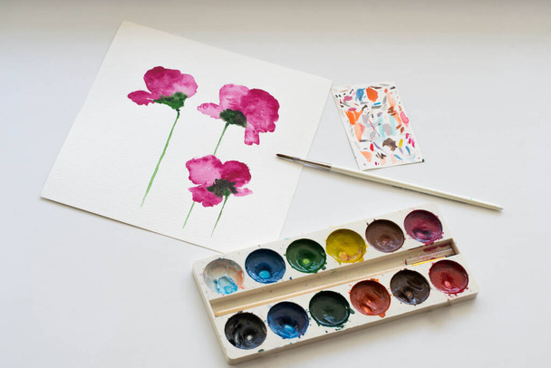 Aquarelverf schilderij van roze magnolia bloem en artistieke gereedschappen op witte tafel. Stillevens samenstelling van de artistieke werkplek - Foto, afbeelding