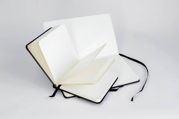 Two black notebooks with blank white pages and dark ribbons bookmarks lie unfold on a white backdrop - Foto, afbeelding