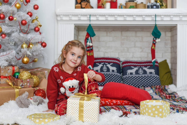 Hyvää joulua ja onnellista joulua! Söpö pieni lapsi tyttö on koristelu joulukuusi sisätiloissa. Onnellinen pieni hymyilevä tyttö joululahjalaatikolla. - Valokuva, kuva