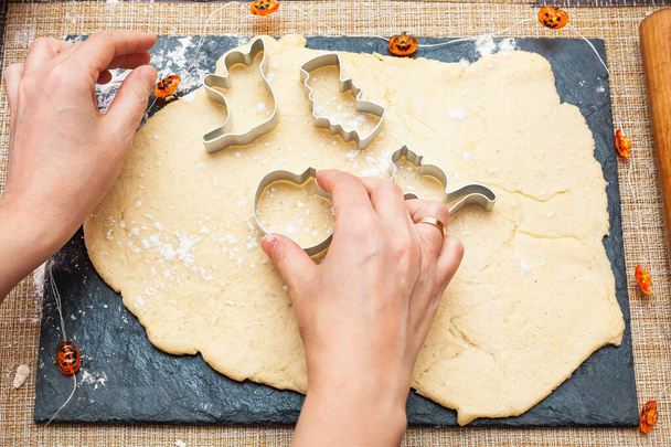 Faire des cookies pour Halloween. Une femme découpe les biscuits de la pâte sous forme de citrouille, chat, fantôme et chauve-souris. - Photo, image