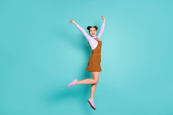Full body photo of excited delightful lucky lady champion hooray jump raise hands breakthrough gesture wear two buns purple sneakers autumn trendy brown mini dress isolated teal color background - Foto, imagen