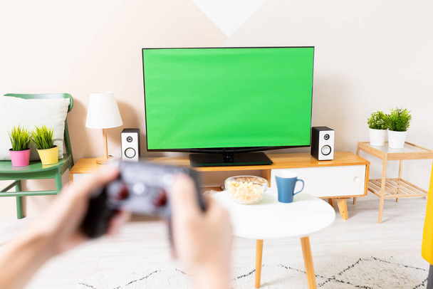 Close up of asian young gamer boy sitting on couch holding wireless controller playing video games on a green chroma key TV screen at home - Photo, Image