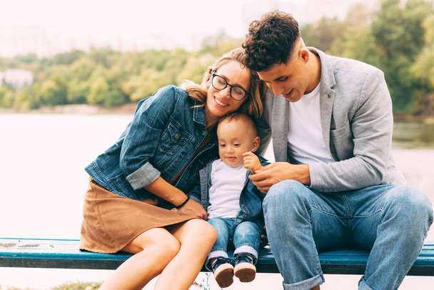 Kiva kuva nuoresta perheestä, jolla on hauskaa penkillä lähellä järveä puistossa - Valokuva, kuva