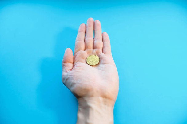 A man holds one coin in his palm, close-up. Fifty cents euro in hand, POV. Bankruptcy, poverty, falling income, low cost. Blue background - Фото, изображение