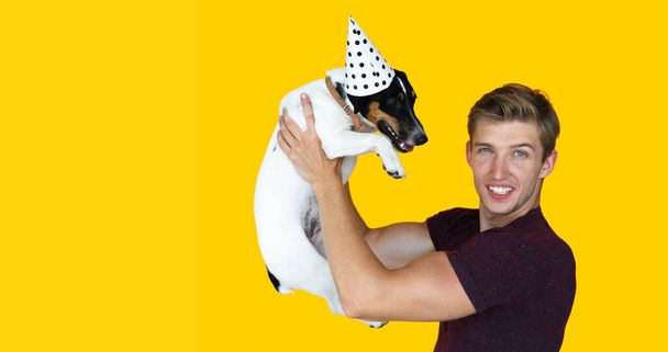 молодой человек европейского внешнего вида на желтом фоне. holding a dog jack Russell raising up - Фото, изображение