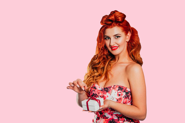 A beautiful girl with red hair on a blue background holds a gift box and looks at the camera. A place for text. Banner. Concept of the holiday - March 8, Valentine's Day, Mother's Day, Girls' Day, International Women's Day, International Women's Day - Photo, Image