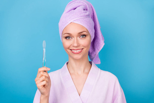 Photo of cute young woman hold toothbrush look camera wear violet towel turban bath robe isolated blue color background - Foto, afbeelding