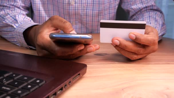 Мужчина держит в руках кредитную карту и пользуется смартфоном для покупок онлайн  - Кадры, видео