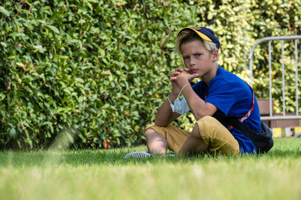 Sochi Russia - 26 sep 2020: boy sitting on the grass in the park on summer day. Child in trendy and cute clothes - Foto, Bild